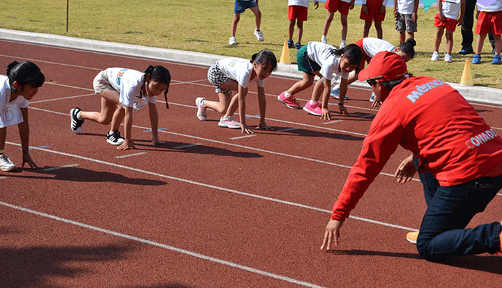 Group of children on a track about to race together as part of an "Estrella Colgate" event.